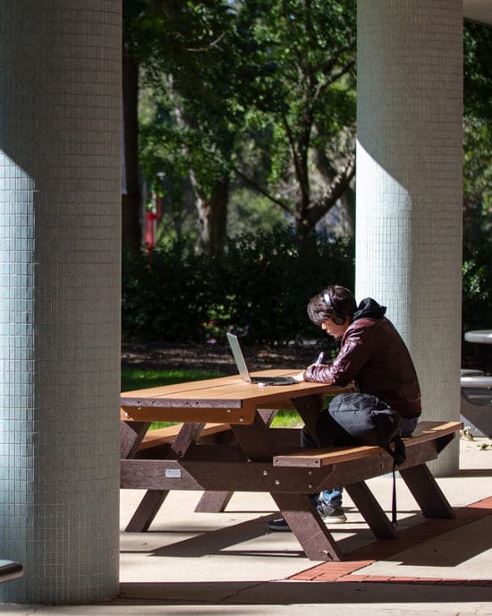 Student sitting on bench with laptop and headphone one