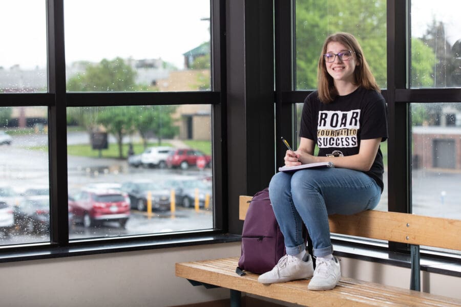 female student sitting in front of window with hands resting on a book on her lap