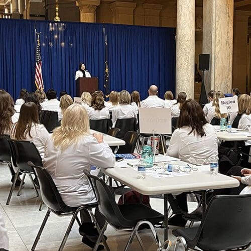 People in white nursing coats sit at white tables in the Indiana statehouse