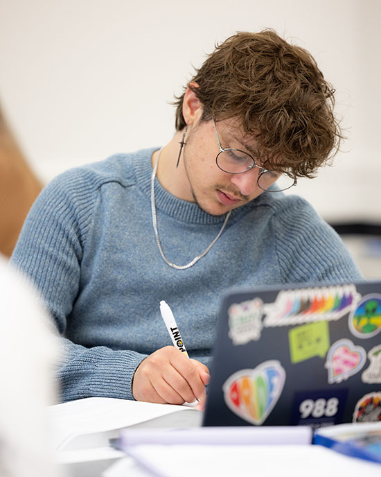 A PNW student works on a laptop in a classroom.