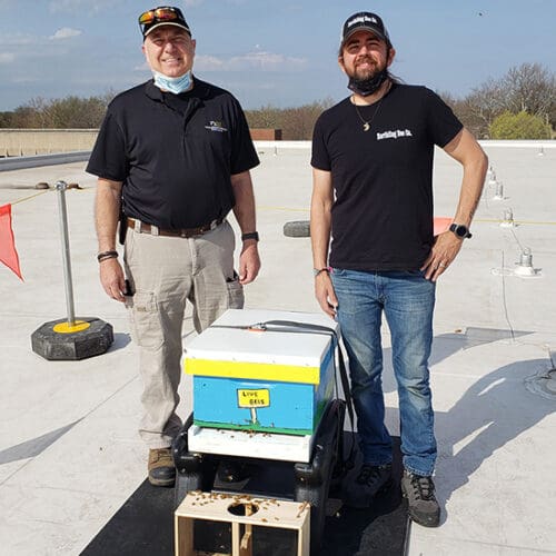 Two men pose with a beehive.