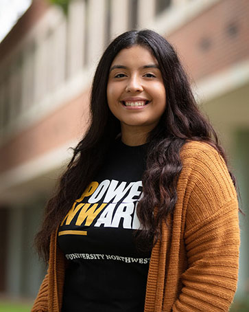 A female student in a Power Onward shirt in front of a PNW building.