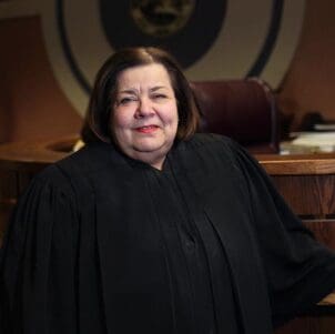 The Honorable Diane Kavadias Schneider poses in judicial robes in a courtroom