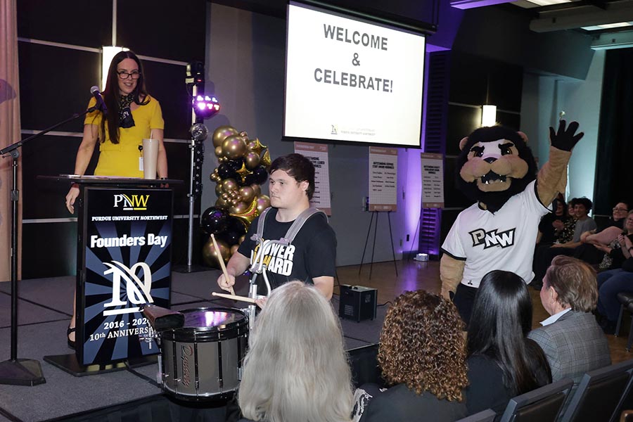 A drummer and PNW mascot Leo march in front of a stage.