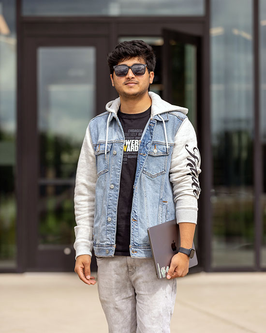 A PNW student in sunglasses stands in front of a building