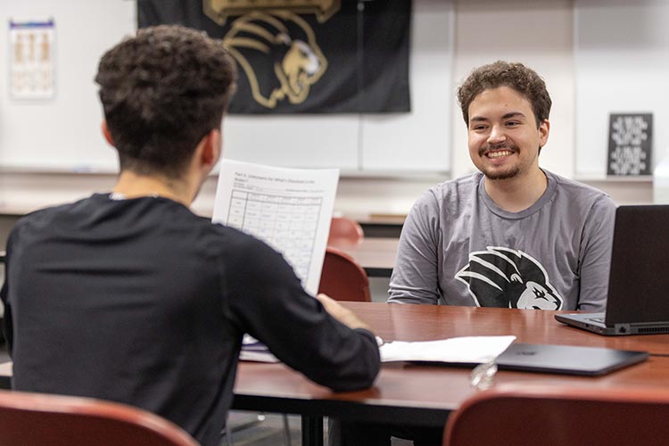 Two PNW students talking together at a table with a laptop in front of them