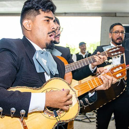 Three men stand and sing while playing guitars