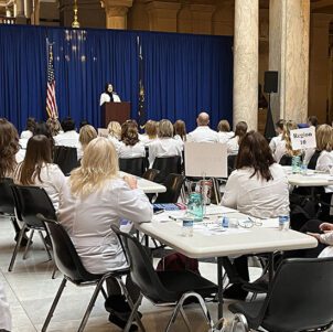 People in white nursing coats sit at white tables in the Indiana statehouse
