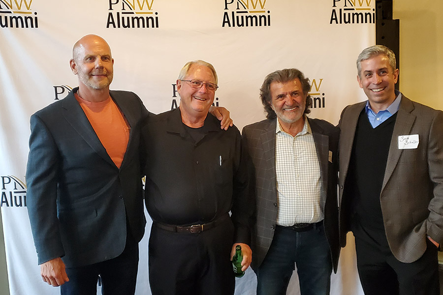 Four people stand together in front of a PNW Alumni backdrop.