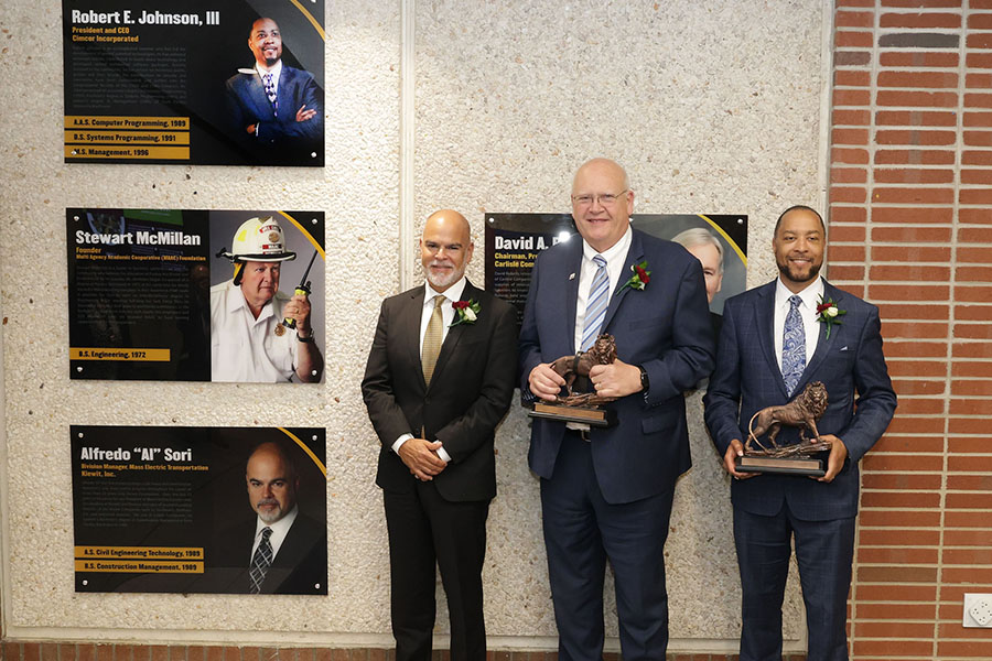 Alfredo "Al" Sori, Stewart "Stu" McMillan, and Robert Johnson III pose next to the Alumni Hall of Fame wall