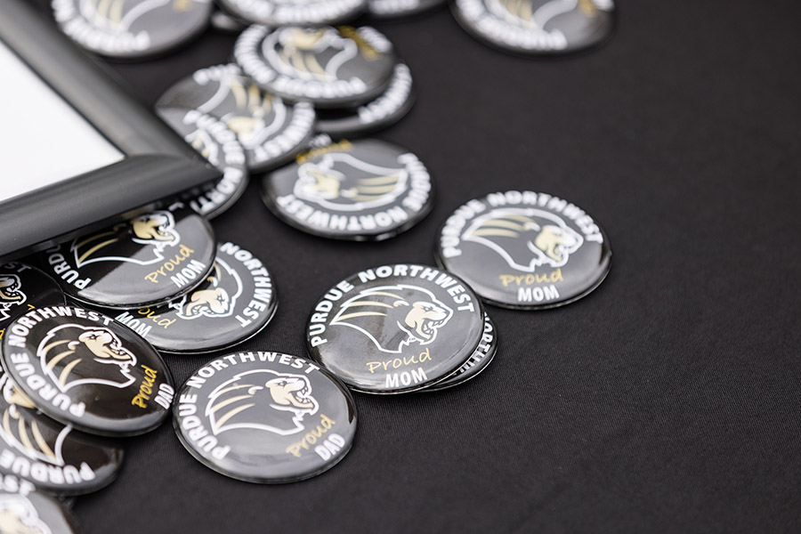 Purdue Northwest "Mom" and "Dad" pins sit on a black table cloth.