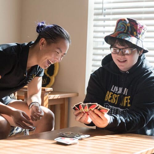 Two students sit at a table. They are playing Uno.