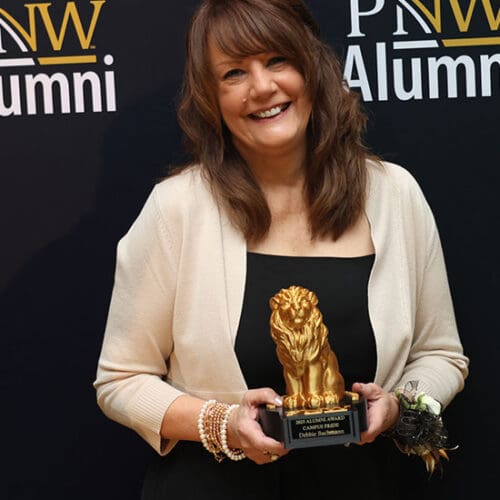 Debbie Bachman poses in front of a PNW Alumni backdrop with her Alumni Award.