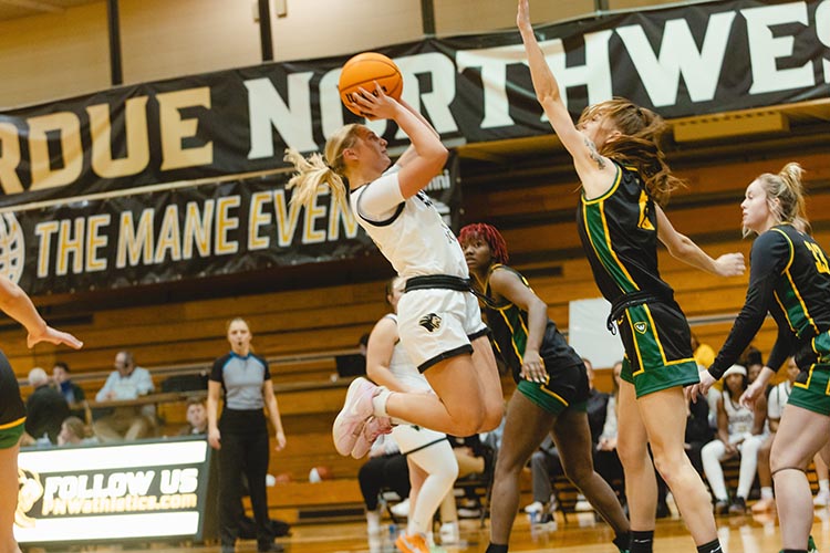 Women's Basketball photo. Player shooting the basketball while opposing team tries blocking it.