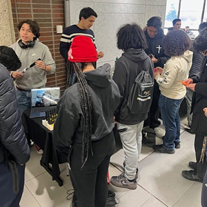 Students stand in front of a table. Their backs are to the camera
