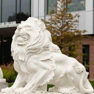 A white lion statue on the PNW Hammond Campus. There is a tree and the Nils Bioscience building in the background.