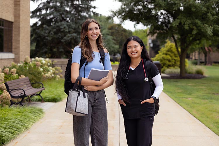 Two students pose together outdoors on PNW's Westville campus. One is wearing nursing scrubs.