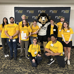 A group of students wearing yellow t-shirts pose together with Leo the Lion.