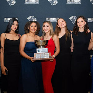 A group of student athletes pose together, holding the Chancellor's Cup.