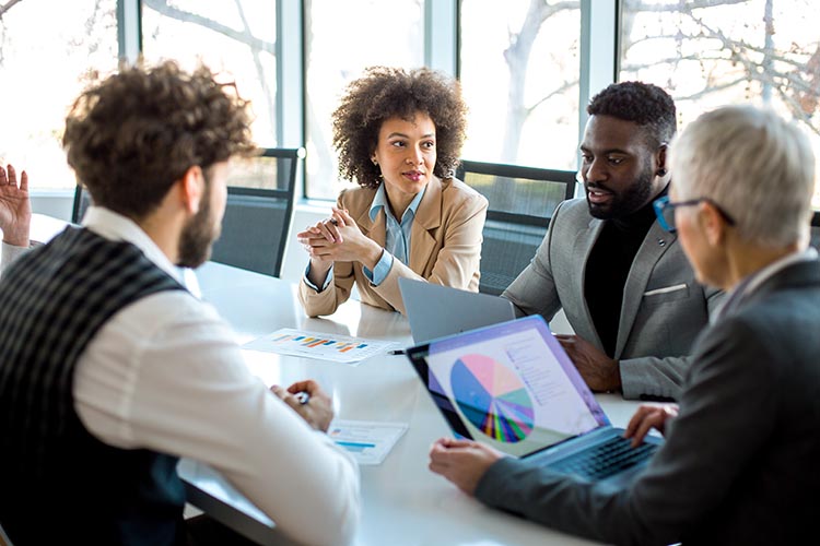Four individuals talking with one another at a table while looking at statistics