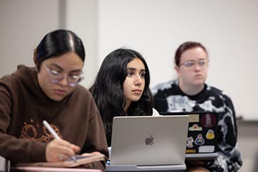 Three PNW students taking notes on their laptops/iPads while listening to the professor 363x242