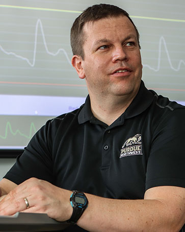 A professor sits in front of a projector screen