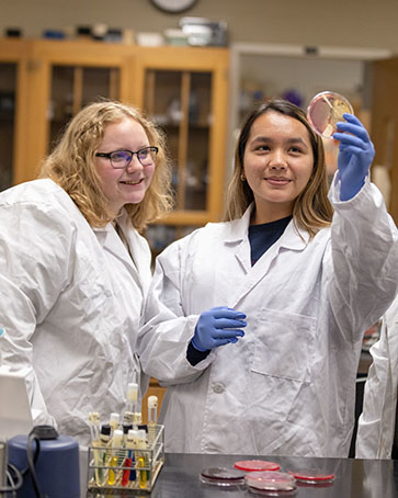 Two students hold a petri dish up to the light