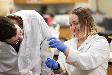 A student in a labcoat looks at a reagent in the lab.