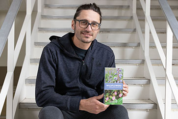 A student on stairs holds a Wildflowers book.