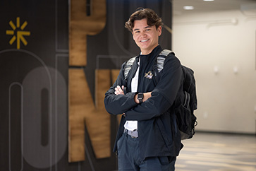 A PNW student stands with their arms crossed in a hallway.