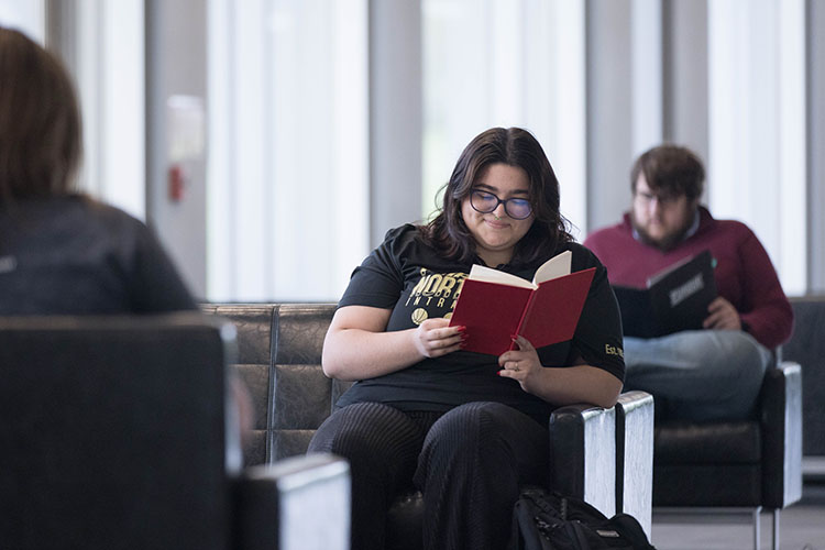 A student sits in a chair and reads a book.