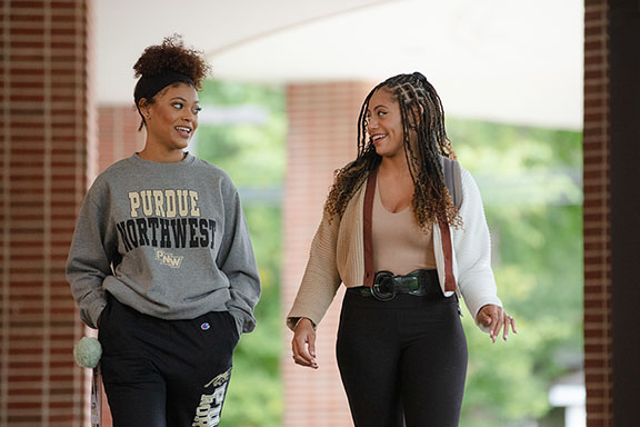 Two students walk together outside. One of them is wearing a Purdue Northwest hoodie, the other is in a cardigan