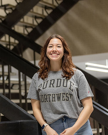 A student in a Purdue Northwest t-shirt poses in front of a staircase