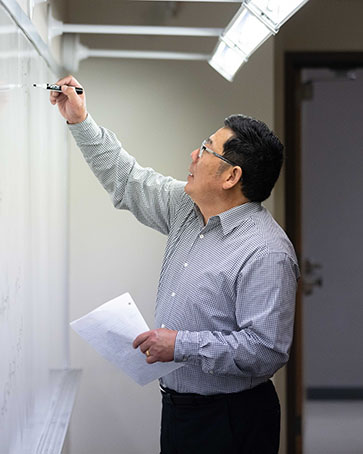 A professor writes on a white board