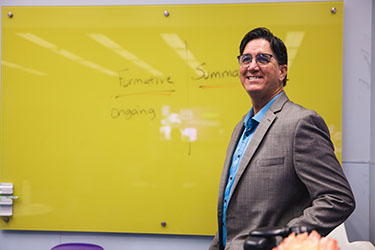 Dave Pratt stands in front of a yellow dry erase board.