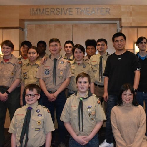 A large group of Boy Scouts in uniform stand together in rows in front of the Immersive Theater at CIVS