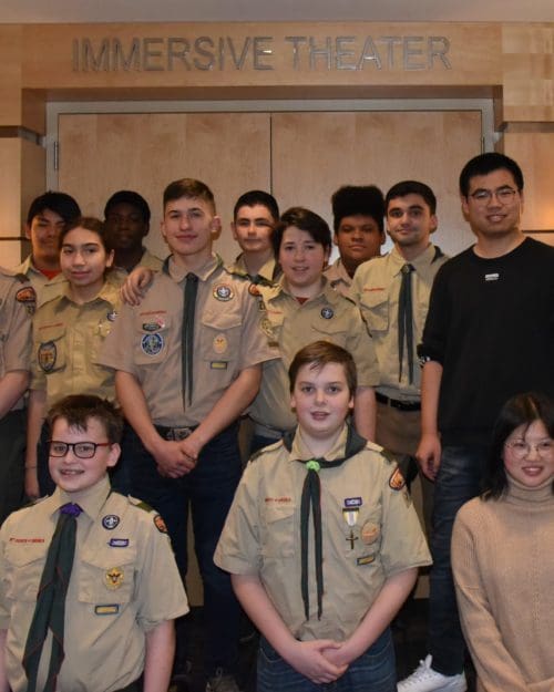 A large group of Boy Scouts in uniform stand together in rows in front of the Immersive Theater at CIVS