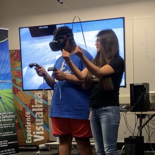 Visitor participates in hands-on experiences of AR & VR projects in the visualization lab. Participant is standing while wearing a tethered VR headset and manipulating had held controllers