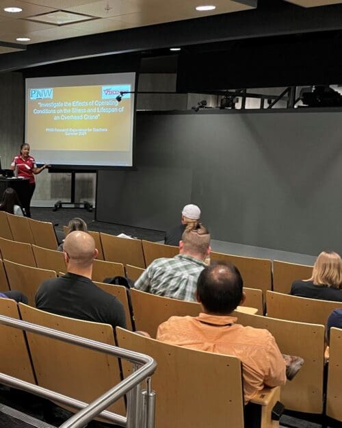 Individual standing and talking in front of screen featuring PowerPoint slide at podium in auditorium