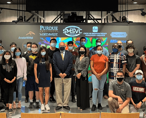 Several people standing in a group in front of large screen featuring several logos at the front of an auditorium