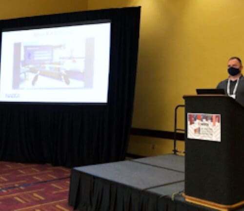 Individual standing in front of screen featuring PowerPoint slide at podium in conference room