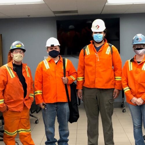 Individuals in conference room wearing bright orange uniform jackets and white hard hats