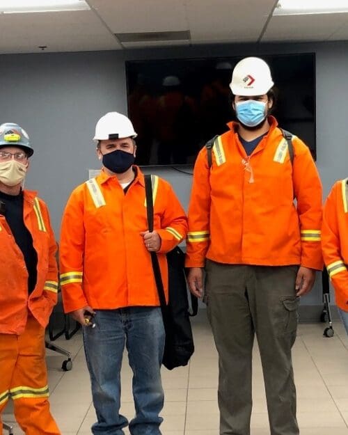 Individuals in conference room wearing bright orange uniform jackets and white hard hats