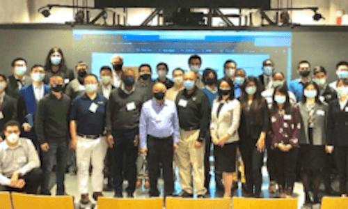 Several people standing in a group in front of large screen featuring several logos at the front of an auditorium