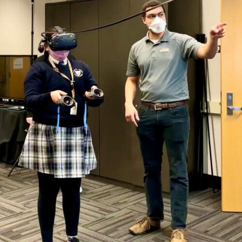 Visitor participates in hands-on experiences of AR & VR projects in the visualization lab. Participant is standing while wearing a tethered VR headset and manipulating had held controllers