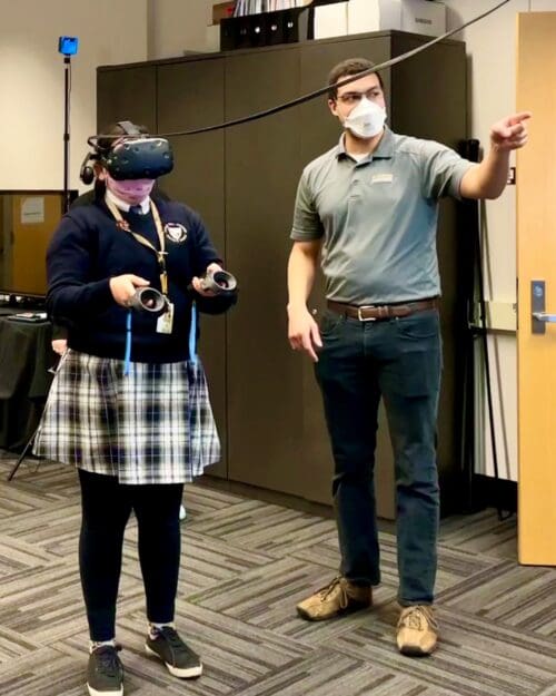 Visitor participates in hands-on experiences of AR & VR projects in the visualization lab. Participant is standing while wearing a tethered VR headset and manipulating had held controllers