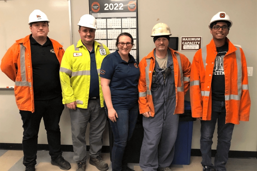 Individuals in conference room wearing bright orange uniform jumpsuits and white hard hats