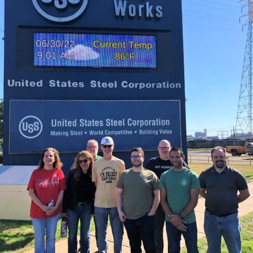 Visitors standing outdoors in front of U.S. Steel Gary Works commercial signage