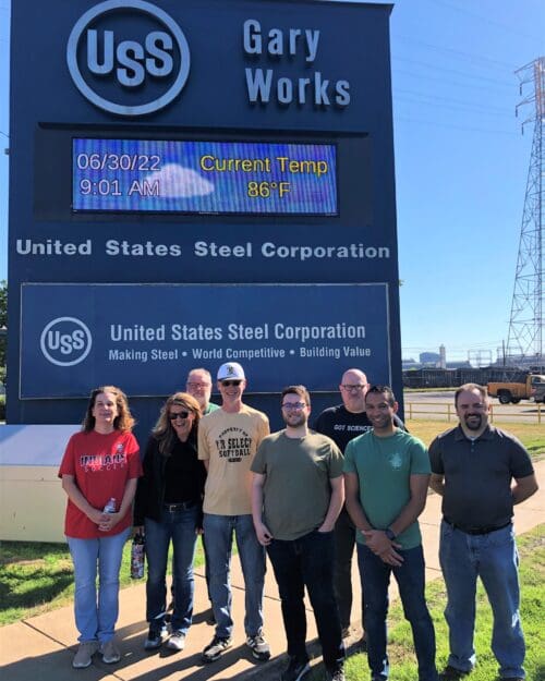 Visitors standing outdoors in front of U.S. Steel Gary Works commercial signage