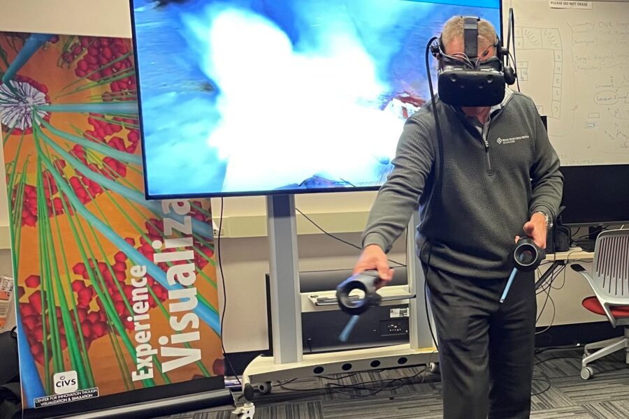 Visitor participates in hands-on experiences of AR & VR projects in the visualization lab. Participant is standing while wearing a tethered VR headset and manipulating had held controllers